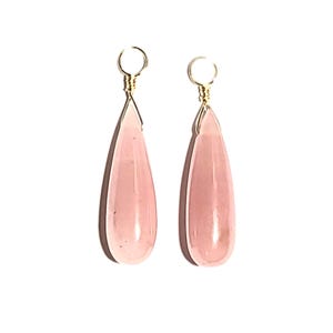 May include: A pair of teardrop-shaped earrings featuring translucent pale pink stones. Each stone is suspended from a small, circular gold-toned wire loop at the top, creating a simple and elegant drop design with a smooth, polished finish.