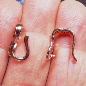 May include: Two rose gold-colored earring hooks are displayed. The hooks have a curved design with a small loop at the bottom and a curved top. The hooks are shown against a skin-toned background.