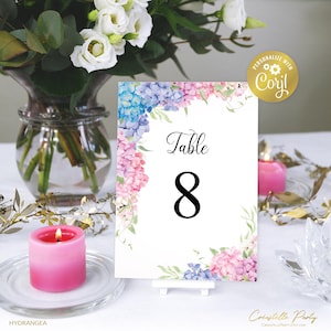 May include: A white table number card with a watercolor floral border in shades of pink, blue, and green. The card says "Table 8" in black text.