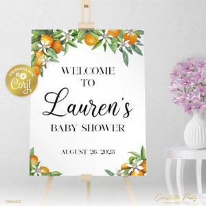 May include: Welcome to Lauren's Baby Shower sign with orange blossoms and leaves. The sign is white with black text and the date August 26, 2023.