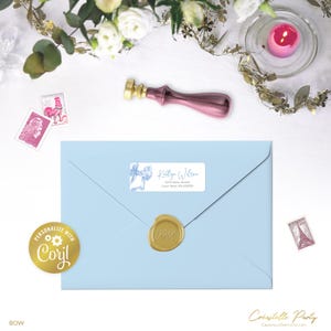 May include: A pale blue envelope with a gold wax seal and a label reading "Kaitlyn Wilson". A pink and gold wax stamp and a gold "Personalize with Corjl" sticker are also present. The word "BOW" is at the bottom.