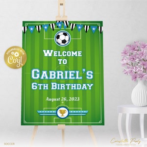 May include: Green and white soccer field welcome sign with a blue banner that says "Welcome to Gabriel's 6th Birthday" and the date "August 26, 2023".