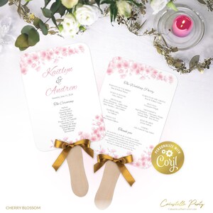 Könnte beinhalten: Zwei rosa und weiße Hochzeitsfächer mit goldenen Schleifen. Die Fächer zeigen ein Kirschblütenmuster und den Text "Kaitlyn & Andrew" und "The Wedding Party".