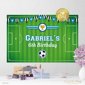 May include: A green and white soccer field backdrop with blue and black pennants. The backdrop has a soccer ball, a trophy, and the text "Gabriel's 6th Birthday".
