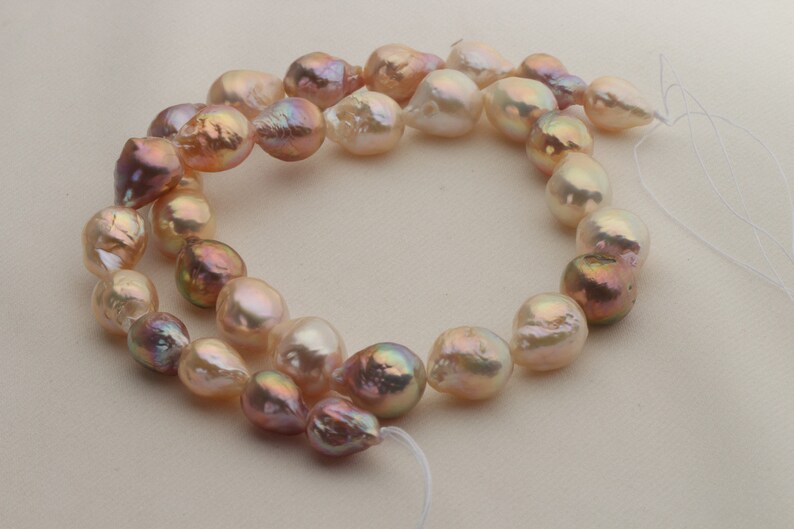 May include: A strand of baroque pearls in shades of pink and white. The pearls are strung on a white thread and have an iridescent sheen.