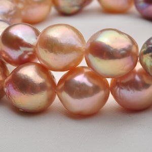 May include: A strand of iridescent pink pearls with a pearlescent sheen. The pearls are round and smooth, and they are strung together on a clear thread.