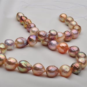 May include: A strand of iridescent baroque pearls in shades of pink, peach, and gold. The pearls are strung on a white cord and are of varying sizes.