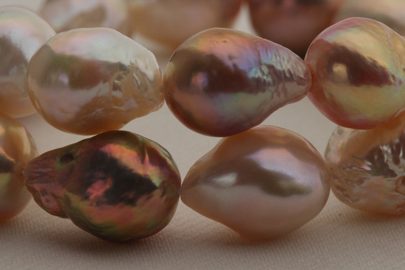 May include: A strand of iridescent pink and white baroque pearls. The pearls are irregular in shape and have a smooth, glossy finish.