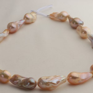 May include: A strand of baroque pearls in shades of pink and peach. The pearls are irregular in shape and have a high luster.