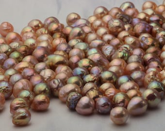 May include: A collection of iridescent pink and green pearls, scattered on a white surface. The pearls are various sizes and shapes, with some having a more irregular, baroque shape.