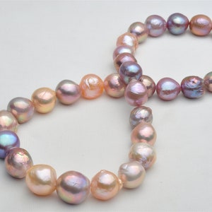 Op de afbeelding: Een streng roze, paarse en perzikkleurige zoetwaterparels. De parels zijn geregen aan een wit koord en zijn gerangschikt in een cirkel.
