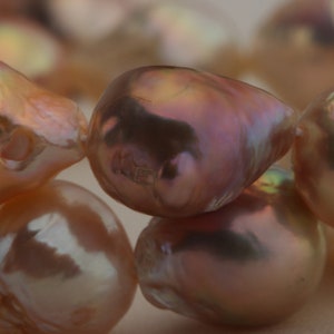 May include: A strand of iridescent pink pearls, each pearl has a unique shape and texture.