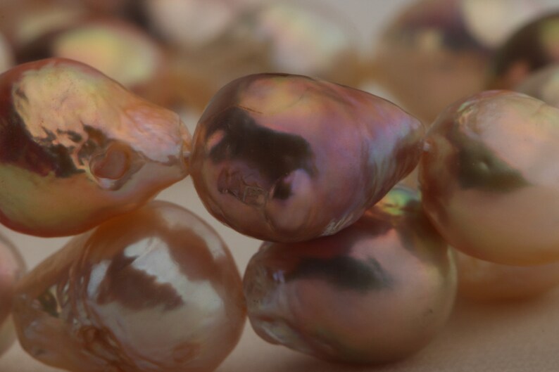 May include: A strand of iridescent pink pearls, each pearl has a unique shape and texture.
