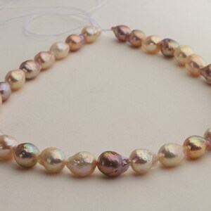 May include: A strand of baroque pearls in shades of pink, white, and gold. The pearls are strung on a white cord and are of varying sizes and shapes.