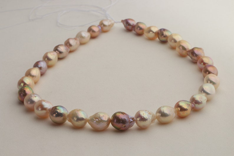 May include: A strand of baroque pearls in shades of pink, white, and gold. The pearls are strung on a white cord and are of varying sizes and shapes.