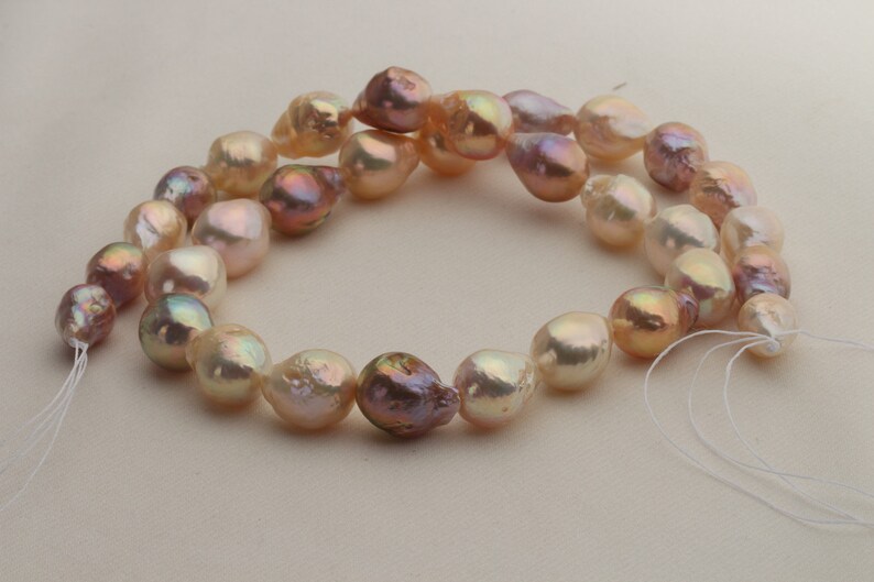 May include: A strand of baroque pearls with a mix of peach, pink, and iridescent colors. The pearls are strung on a white thread and have a natural, irregular shape.