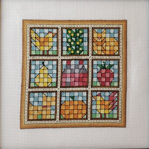 Könnte beinhalten: Ein gerahmtes Kreuzstichstück mit einem Patchwork-Design, das eine Vielzahl von bunten Bildern zeigt, darunter einen Vogel, ein Haus, eine Birne, eine Erdbeere, einen Kürbis und eine Katze.