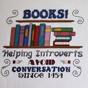 May include: Cross-stitch embroidery featuring the text "BOOKS! Helping Introverts Avoid Conversation Since 1454" and a depiction of a bookshelf with books.