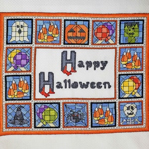 May include: A cross-stitch design with a colourful orange, yellow, and blue border. The centre of the design features the words "Happy Halloween" in black letters. The border is filled with various Halloween-themed images, including ghosts, pumpkins, candy corn, and bats.