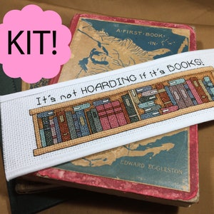 Op de afbeelding: Witte kruissteek-bladwijzer met een boekenkastontwerp en de tekst "Het is geen hamsteren als het boeken zijn!" De bladwijzer ligt op een vintage boek met een kaart op de omslag.