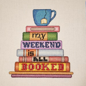 May include: A stack of colourful books with a blue teacup on top. The books have the words "my weekend is all booked" on them.