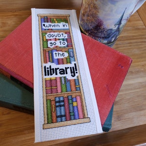 Może przedstawiać: Biała zakładka haftowana krzyżykiem z wzorem biblioteki i tekstem "When in doubt, go to the library!"