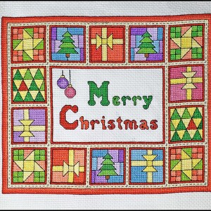 May include: A red and white cross-stitch pattern with a patchwork design. The center of the pattern features the words "Merry Christmas" in green and red letters. The pattern is surrounded by a border of small squares with different designs.