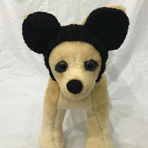 May include: A small, tan dog wearing a black knitted Mickey Mouse hat with large ears.