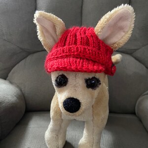 May include: A plush toy dog wearing a red knitted hat with a button on the side.
