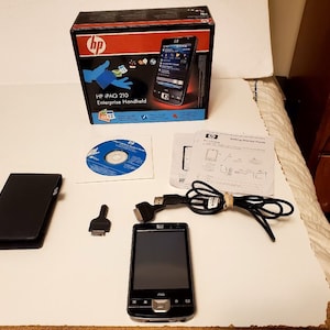 May include: A black HP iPAQ 210 Enterprise Handheld PDA with a black case, a CD, a stylus, a USB cable, and a manual. The PDA has a screen that is on and shows a menu.