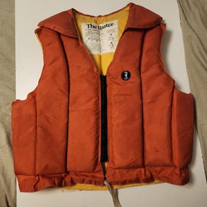 Peut inclure: Un gilet de sauvetage orange et jaune avec une fermeture éclair noire et un logo d'hippocampe. Le gilet porte une étiquette indiquant "The Water". Ce gilet de sauvetage vintage est conçu pour la sécurité aquatique.