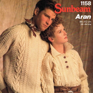 May include: Cream-coloured Aran knit sweaters. One is a crew neck, the other a collared button-up. The image includes the text "Sunbeam Aran" and measurements of 86-112 cm. The sweaters have a cable knit design.