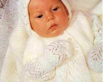Könnte beinhalten: Ein Baby in einem weißen Strick-Set, bestehend aus einer Kapuzenjacke, Fäustlingen und einer Mütze. Das Outfit hat ein zartes Lochmuster und wird vorne mit Knöpfen geschlossen. Der Text "Snuggly 3ply" und "c3421 14-18" ist ebenfalls enthalten.