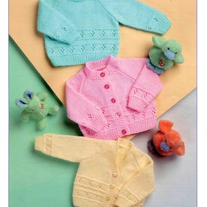 Puede incluir: Imagen de suéteres para bebés en azul claro, rosa y amarillo. Los suéteres tienen patrones decorativos y cierres de botones. La imagen también incluye pequeños juguetes de peluche. El texto "Wondersoft DK" y "Stylecraft" es visible.