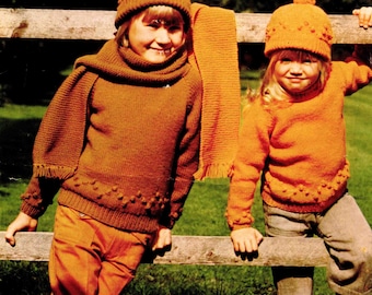 May include: Vintage Patons Aran Style knitting pattern cover featuring two children wearing matching orange and brown knitwear. The children are wearing hats, sweaters, scarves, and pants. The text on the cover reads "Patons Aran Style" and "Capstan 24-34 in."