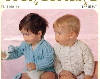 Könnte beinhalten: Vintage Sirdar Wonderland Strickmuster-Cover mit zwei Babys in Strickjacken. Ein Baby trägt eine hellblaue Strickjacke, das andere eine weiße. Das Cover trägt die Aufschrift "Sirdar Wonderland" und "12/18 Monate".
