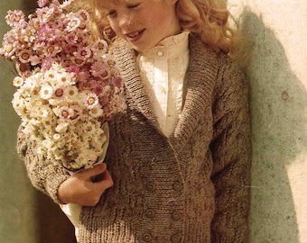 May include: A young person wearing a brown tweed cardigan with a red plaid skirt, holding a bouquet of pink and white flowers. The image includes text that reads "Patons Waverley DK Tweeds". The cardigan has a double-breasted design.