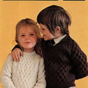 Könnte beinhalten: Zwei Kinder tragen Strickpullover mit einem Zopfmuster. Das Mädchen trägt einen weißen Pullover und der Junge einen braunen Pullover. Das Bild stammt aus einem Strickmusterbuch und enthält den Titel "a Harmony pattern Aran style" und die Nummer "183". Die Größen sind mit "20" - "28" angegeben.