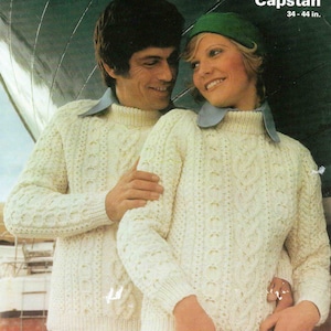 Puede incluir: Dos personas vistiendo suéteres de punto blanco con trenzas. La mujer lleva un sombrero verde y el hombre lleva un cuello azul. Los suéteres son ambos de estilo Aran y el texto "Capstan 34-44 in." es visible.