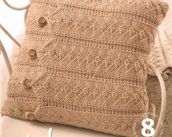 May include: A beige knitted pillow with a buttoned closure, resting on a white chair. The pillow features a textured pattern and is part of a home decor collection. The word "Home" is visible in the image.