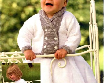May include: A baby wearing a white knitted cardigan with gray trim and a matching hat. The cardigan has a double-breasted design with white buttons. The baby is also wearing a white dress. The image includes the text "Peter Pan Moondust".