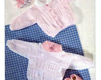 May include: A light pink knitted baby cardigan with a white collar and matching buttons. The cardigan is displayed with a matching knitted sweater and pink baby shoes. The image also includes two small bunny dolls.