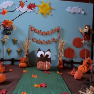 May include: A felt craft scene with an owl, scarecrow, and pumpkins. The scene is decorated with fall leaves, a banner of pumpkins, and a sun.