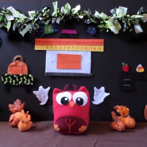 May include: A felt Halloween-themed play set with a red owl, pumpkins, and a fireplace. The set includes a number line, a felt fireplace, and a felt owl with white wings.
