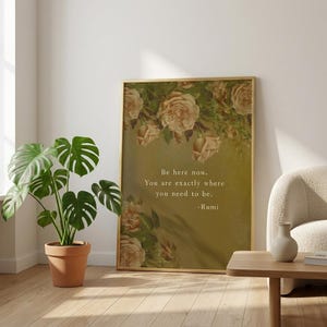 Op de afbeelding: Een ingelijste kunstprint met een gouden lijst met een bloemenontwerp en de quote "Be here now. You are exactly where you need to be. -Rumi." De print heeft een vintage esthetiek met een warm kleurenpalet.