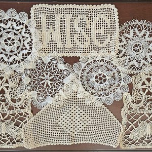 May include: A collection of off-white crocheted lace doilies in various shapes and sizes, including circular, rectangular, and square pieces. One rectangular piece features the word "WISE" woven into the center of the intricate thread pattern.