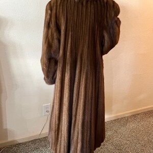 May include: A long brown fur coat with a collar and a pleated design. The coat is on a mannequin.