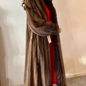 May include: A long brown fur coat with a shawl collar. The coat is lined with a black fabric and has a red lining.