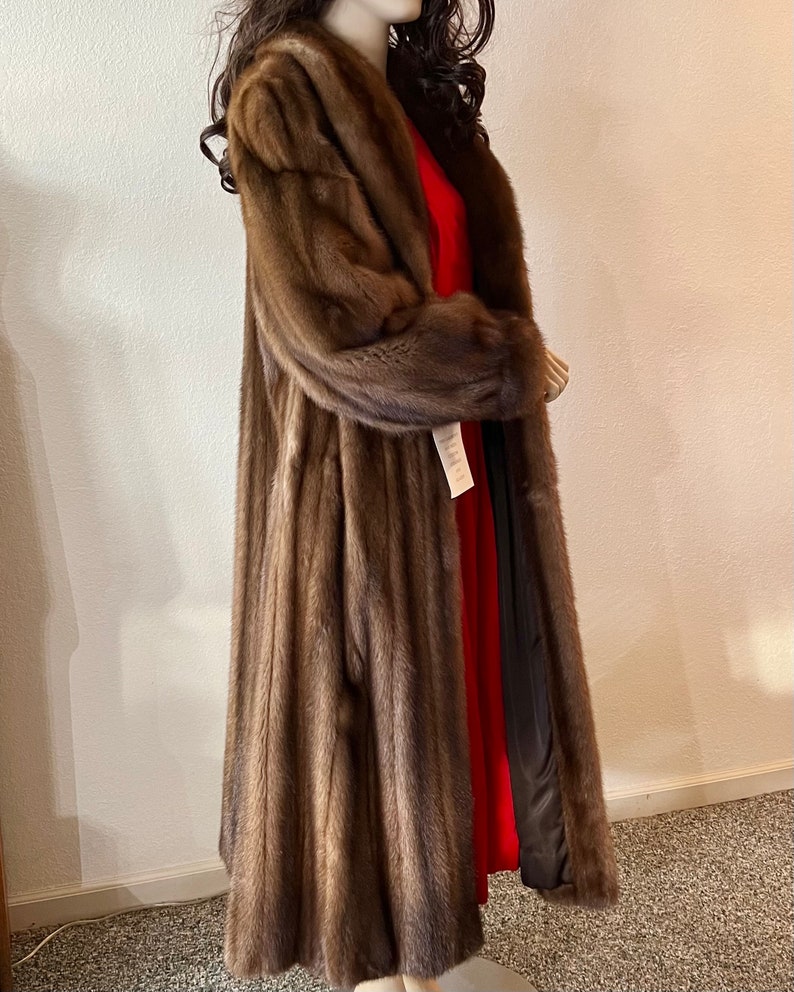 May include: A long brown fur coat with a shawl collar. The coat is lined with a black fabric and has a red lining.