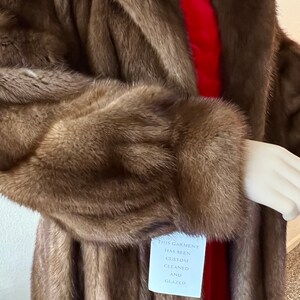 May include: A long brown fur coat with a red lining. The coat has a tag that reads "This garment has been custom cleaned and glazed."